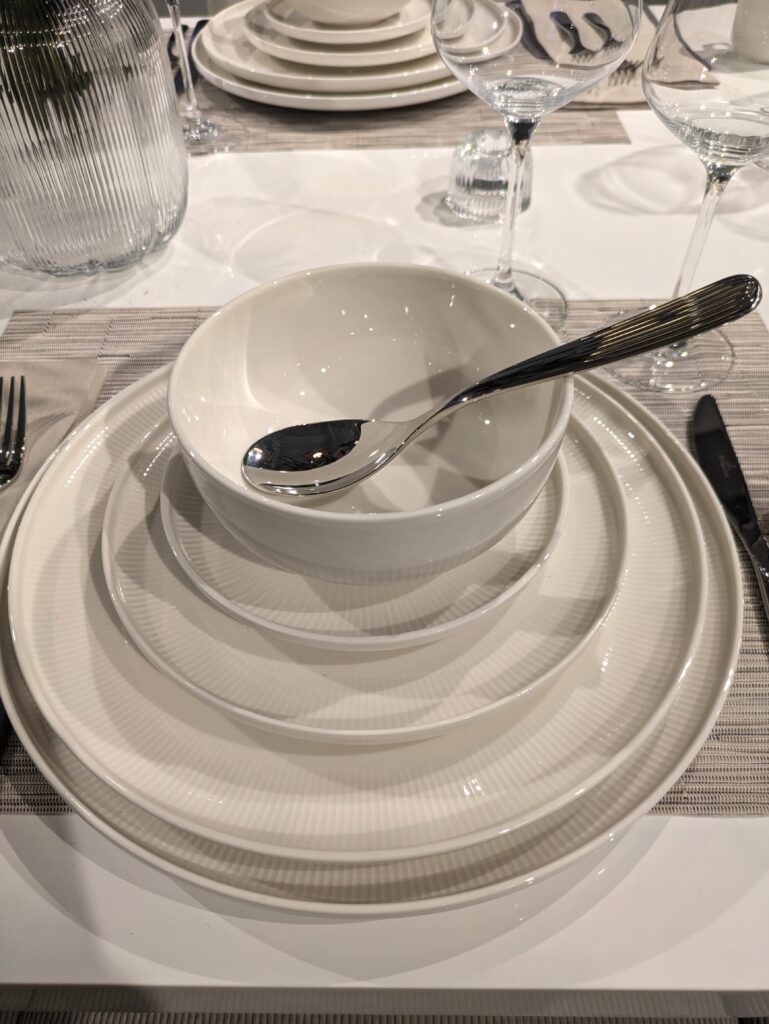 White ceramic dinnerware stack on a white table with a grey textured runner. 